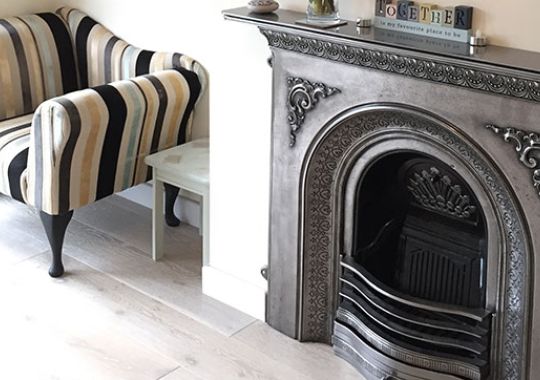 A classic striped armchair beside an ornately carved fireplace, showcasing refined restoration