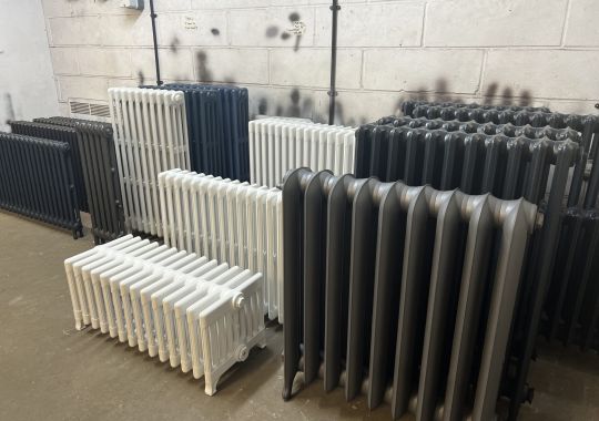 An assortment of freshly painted radiators in black, white, and grey, lined up in a workshop.