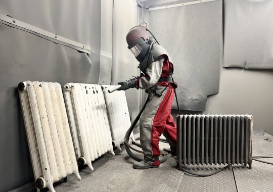 Professional in protective gear spray painting radiators at Blast Spray Polish workshop.